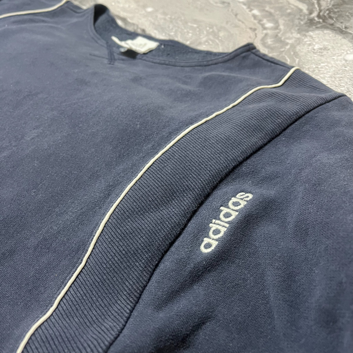 Détail du sweat Adidas bleu marine avec logo brodé et passepoil blanc