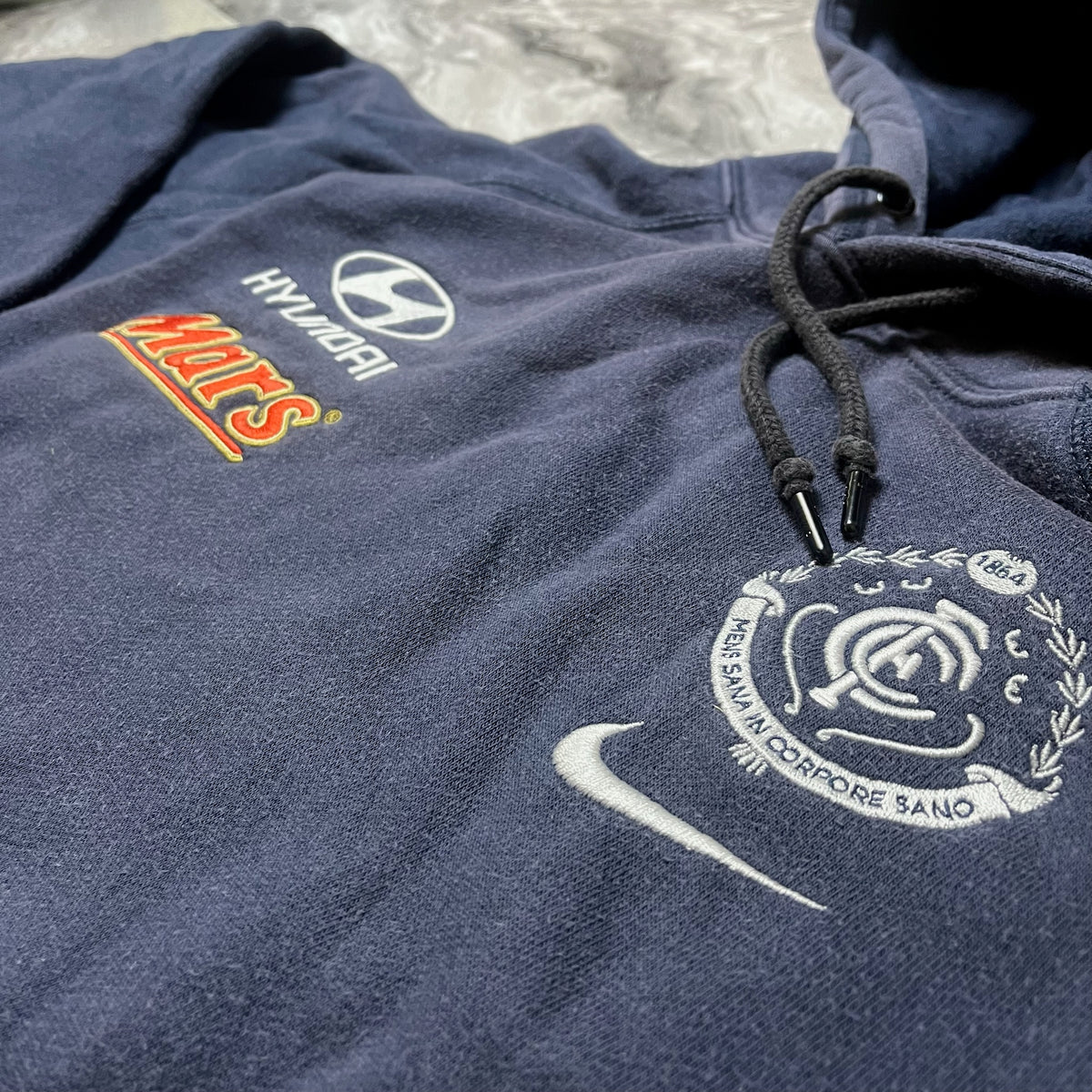 Détail des logos Nike, Hyundai et Mars sur sweat bleu marine
