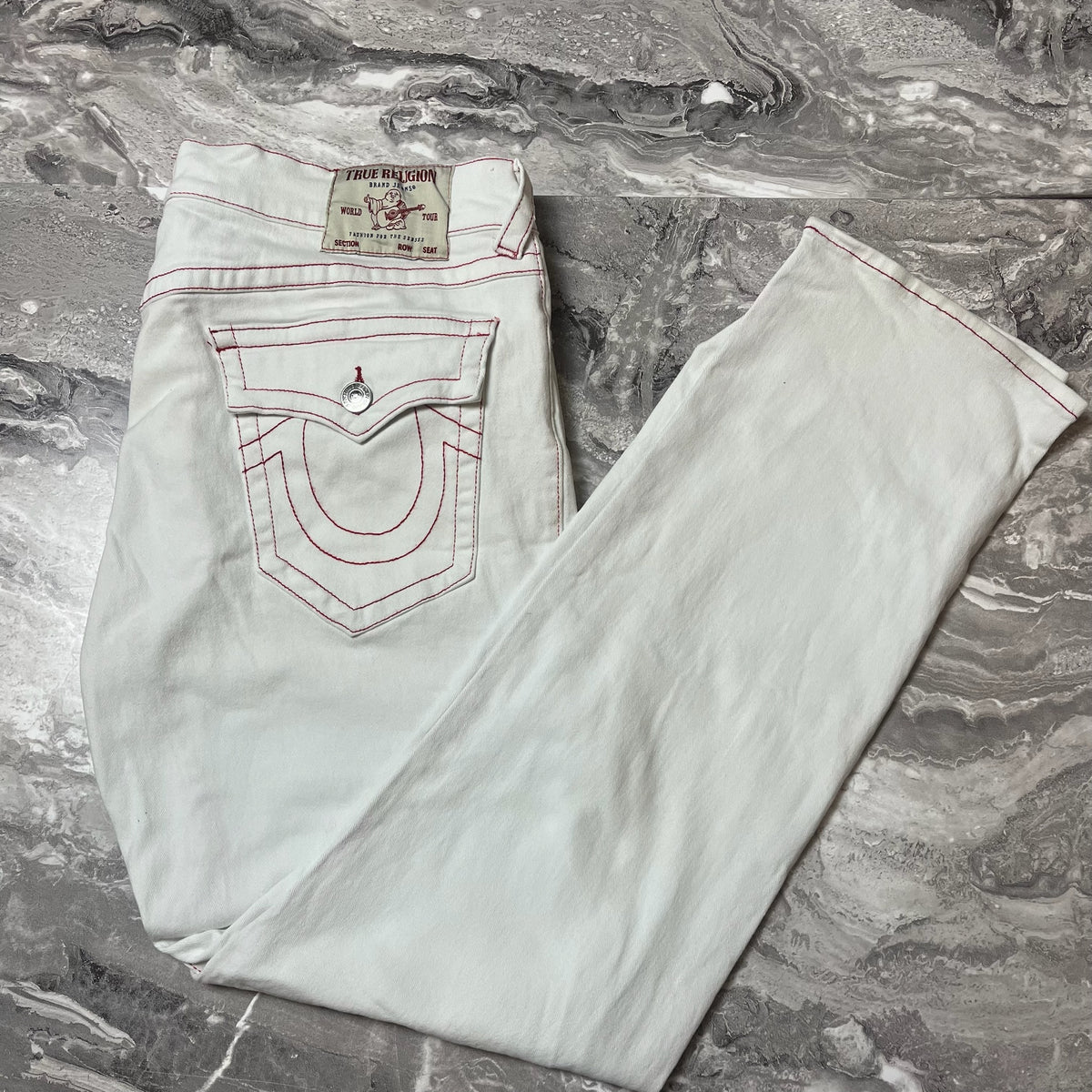 Jean True Religion blanc avec surpiqûres rouges plié sur marbre