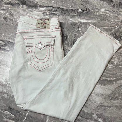 Jean True Religion blanc avec surpiqûres rouges plié sur marbre