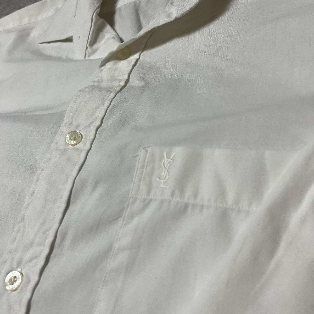 Détail du logo brodé YSL sur la poche de la chemise blanche Yves Saint Laurent