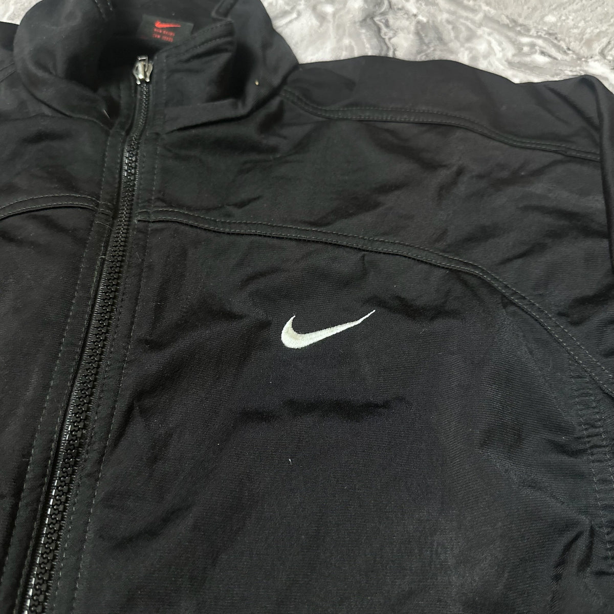 Détail logo Nike blanc brodé sur la poitrine de la veste noire