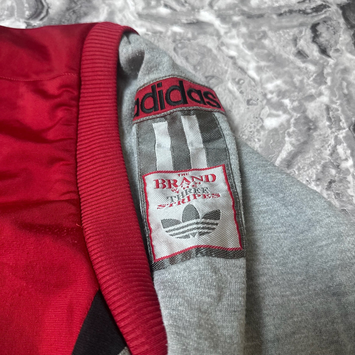 Détail du patch Adidas Brand of the Three Stripes sur la manche grise