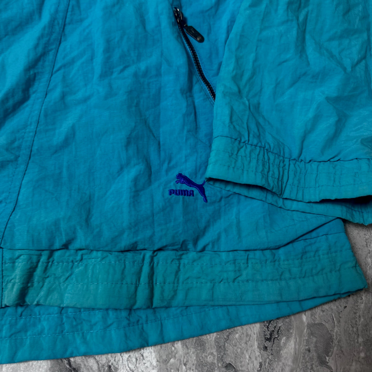 Détail du logo Puma brodé près de la poche de la veste bleue