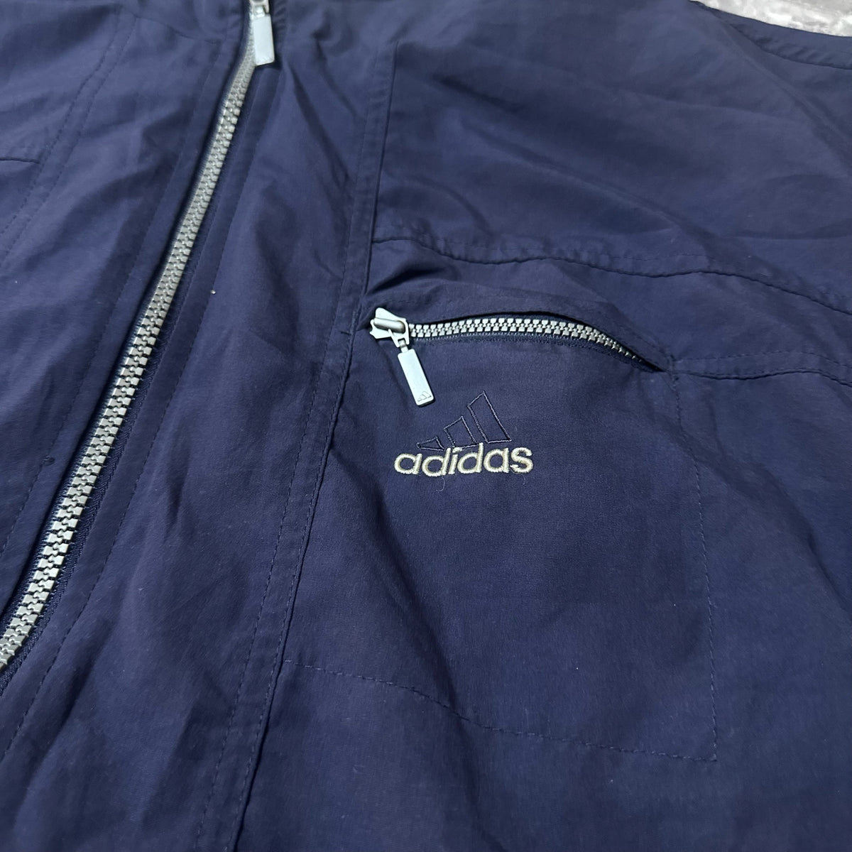 Détail de la poche zippée et broderie logo Adidas sur la veste bleu marine