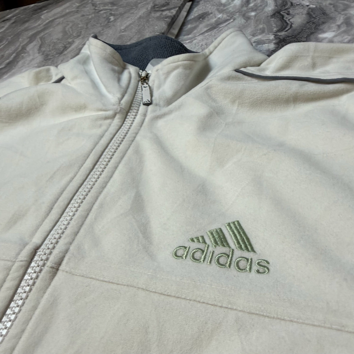 Détail du logo Adidas brodé vert clair sur la veste blanche