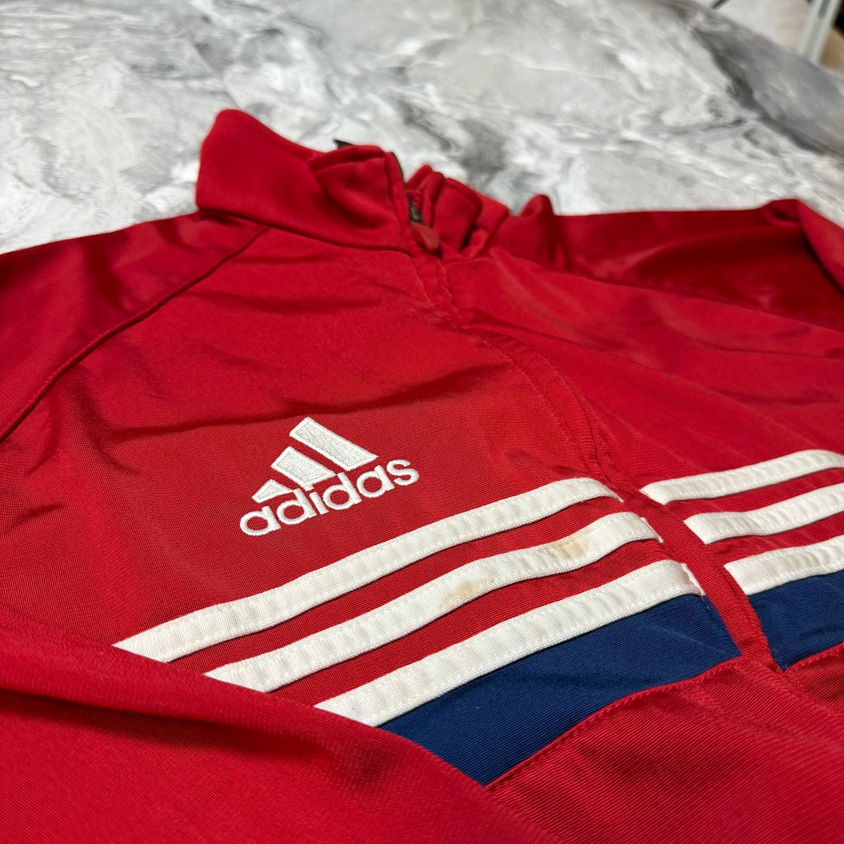 Détail des bandes blanches et bleues et logo Adidas brodé sur le sweat rouge
