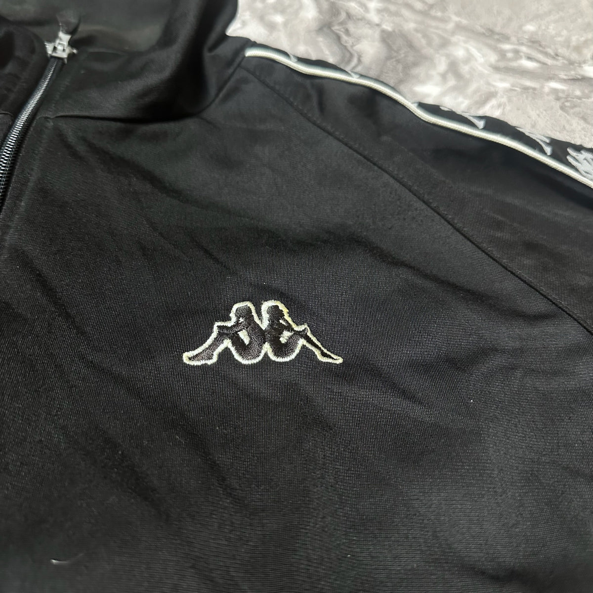 Détail du logo Kappa brodé sur la poitrine de la veste noire